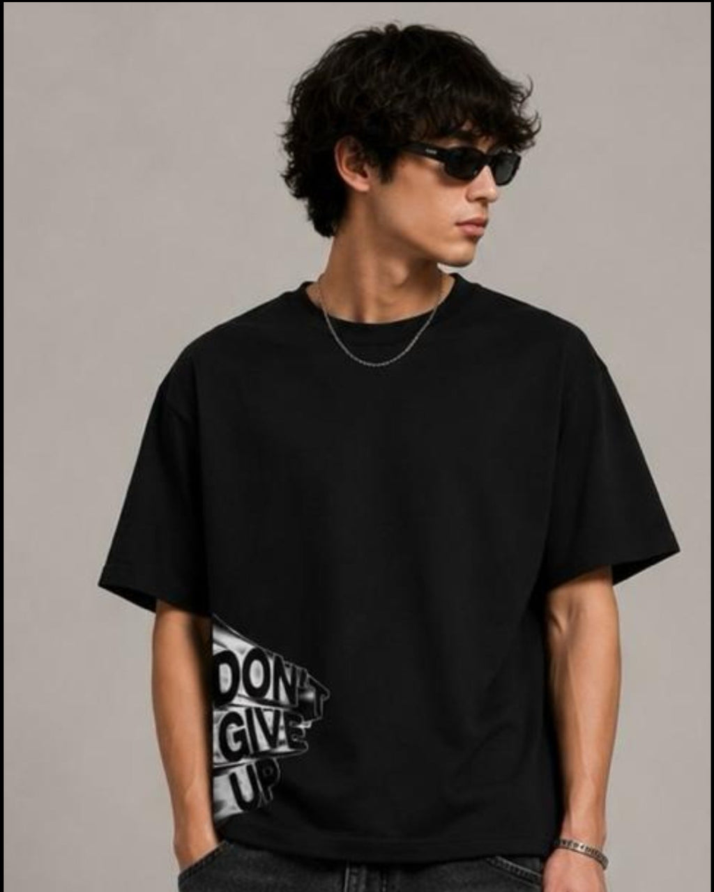 Person wearing a black t-shirt and jeans, holding a black bag against a neutral background