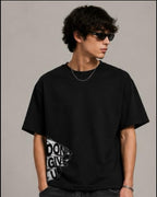Person wearing a black t-shirt and jeans, holding a black bag against a neutral background