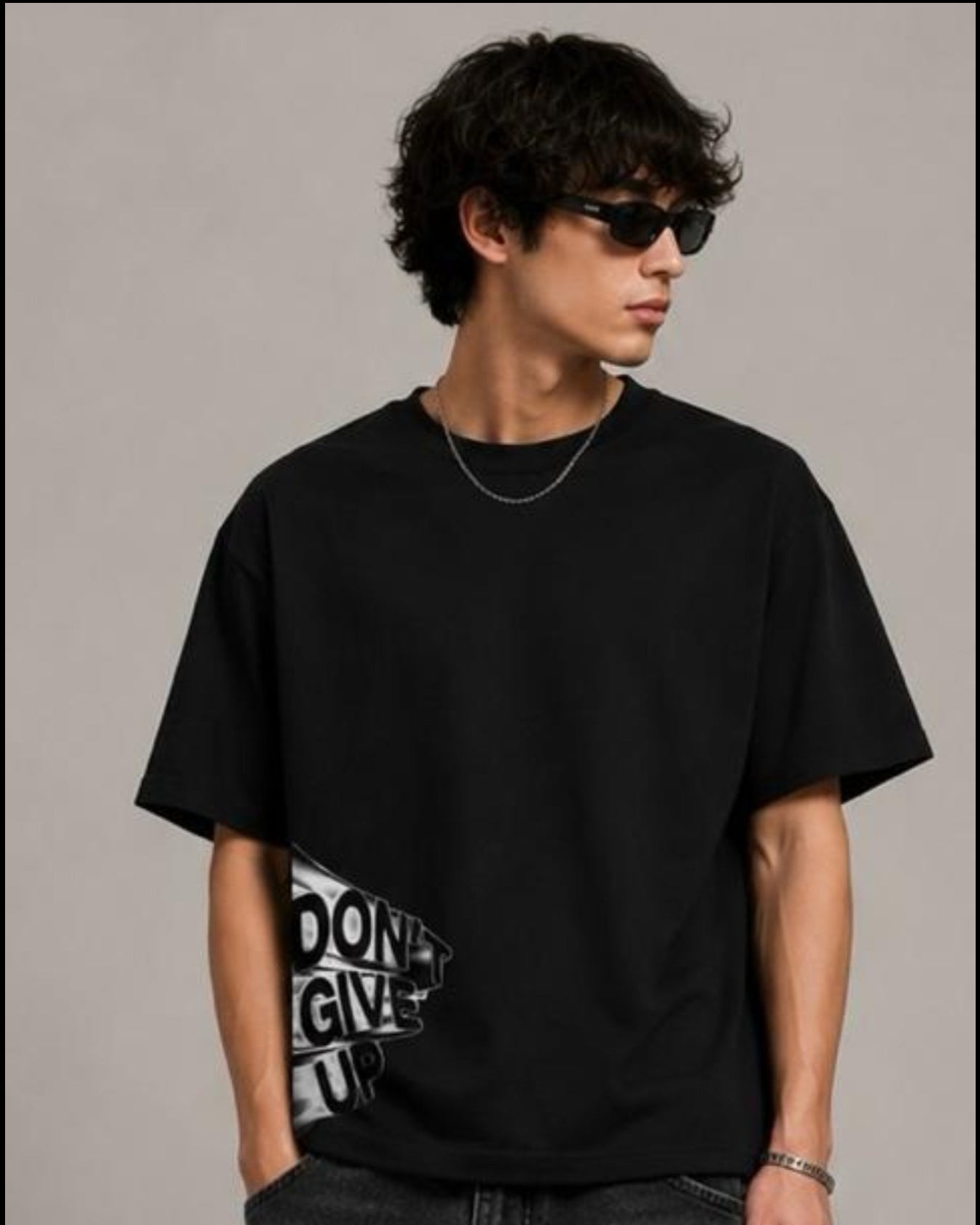 Person wearing a black t-shirt and jeans, holding a black bag against a neutral background